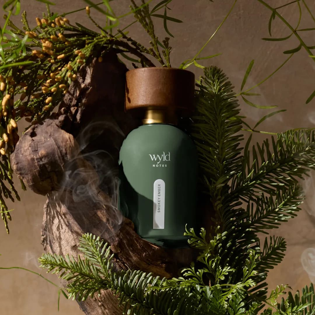 Smokey Ember de Wyld Notes entre des branches de conifères et une fumée légère