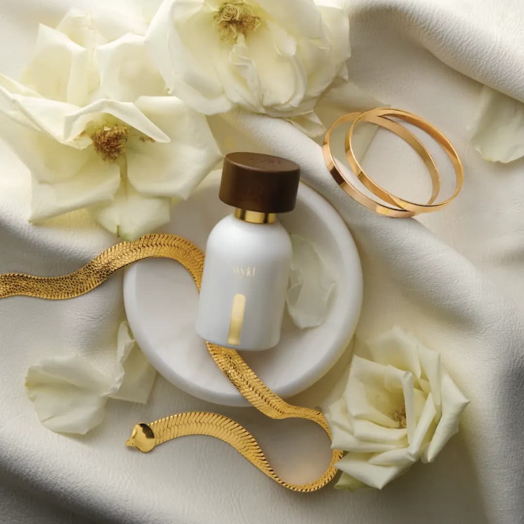 White Lie de Wyld Notes posé entre des roses blanches et un bracelet doré